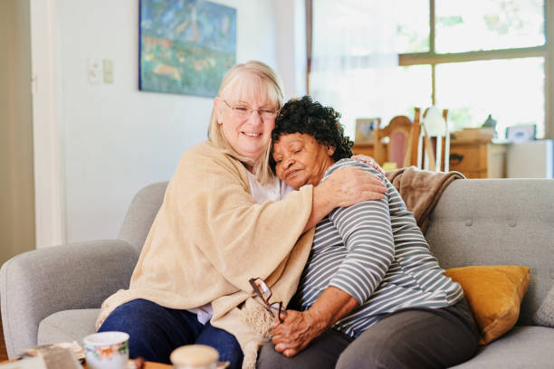 Caregiver and elderly client hugging on couch